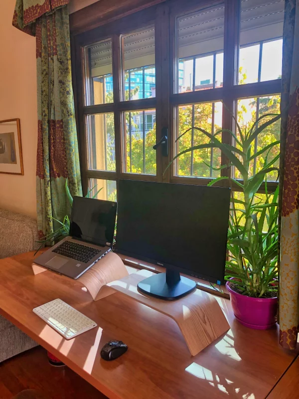 Pencerenin önünde dizüstü bilgisayar ve ahşap monitör içeren bir masa.